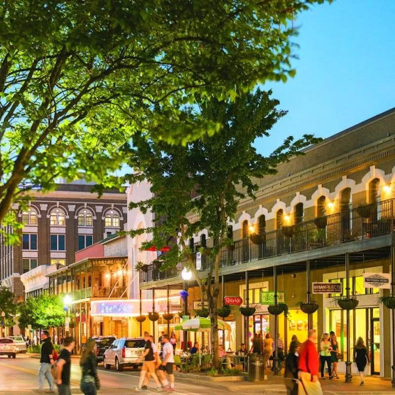 Historic downtown Pensacola street at dusk with lit storefronts and pedestrians